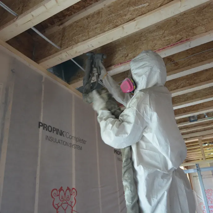 A cropped photo of a Blouin Brothers technician installing sheets of pink insulation prior to installing drywall.